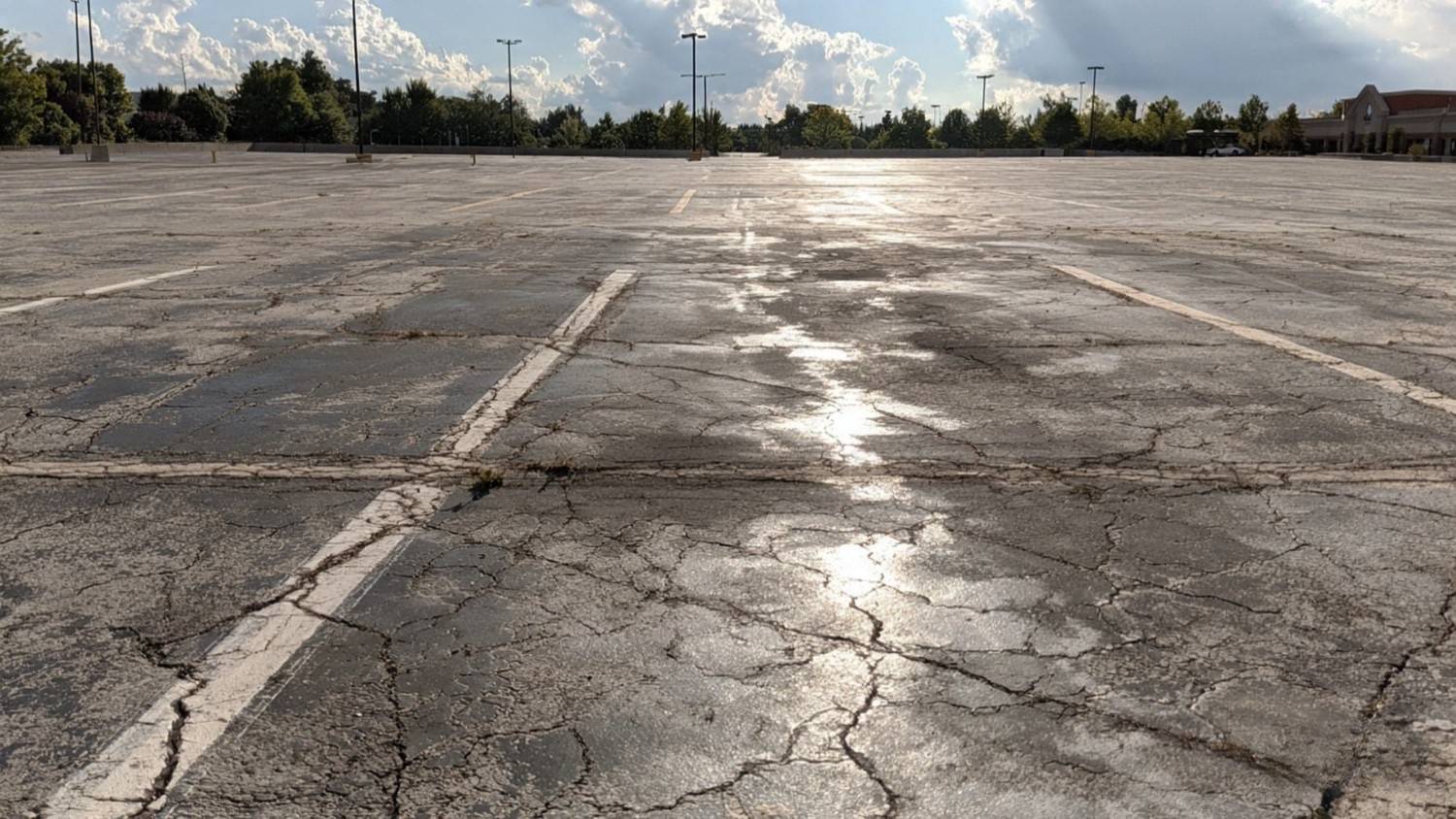 Cracked and weathered commercial parking lot with faded pavement markings and widespread surface deterioration, illustrating how heat, heavy traffic, and seasonal wear contribute to asphalt damage in New England summers.