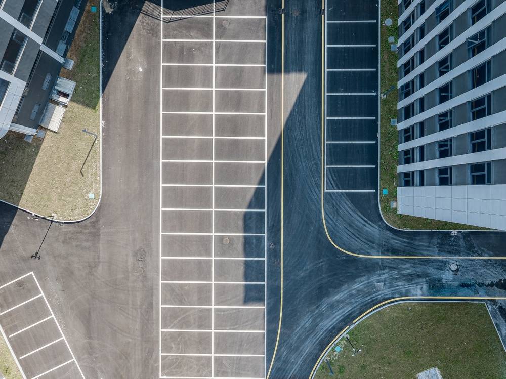 Aerial view of a commercial parking lot with freshly applied pavement markings and parking stall striping, showing clearly defined traffic lanes, directional guidance, and organized parking spaces surrounding a modern office building.