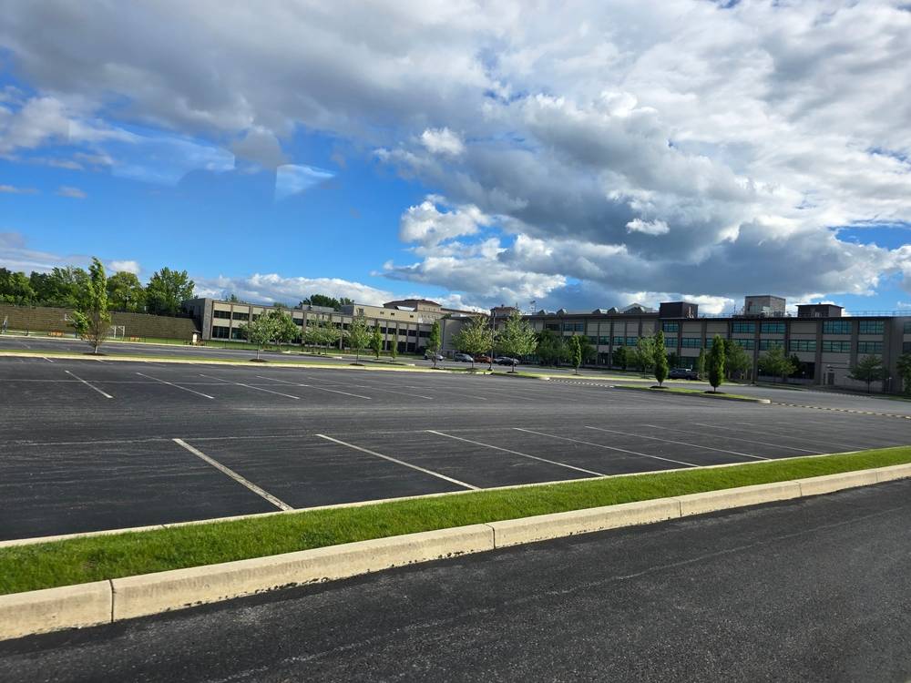Freshly paved commercial parking lot during summer with smooth asphalt surface, parking lines, and office buildings under bright skies before peak heat conditions.
