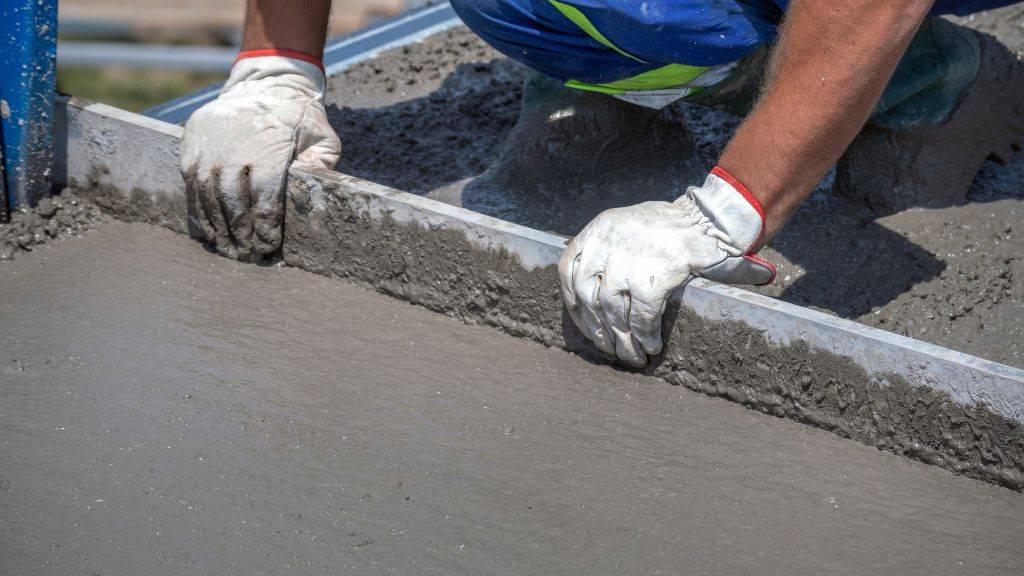 Construction mason screeding and smoothing wet concrete during early fall commercial concrete sidewalk repairs