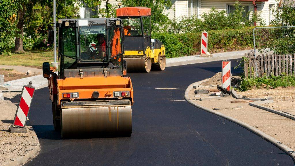 Road roller compacting fresh asphalt pavement during pre-winter commercial maintenance in New England.