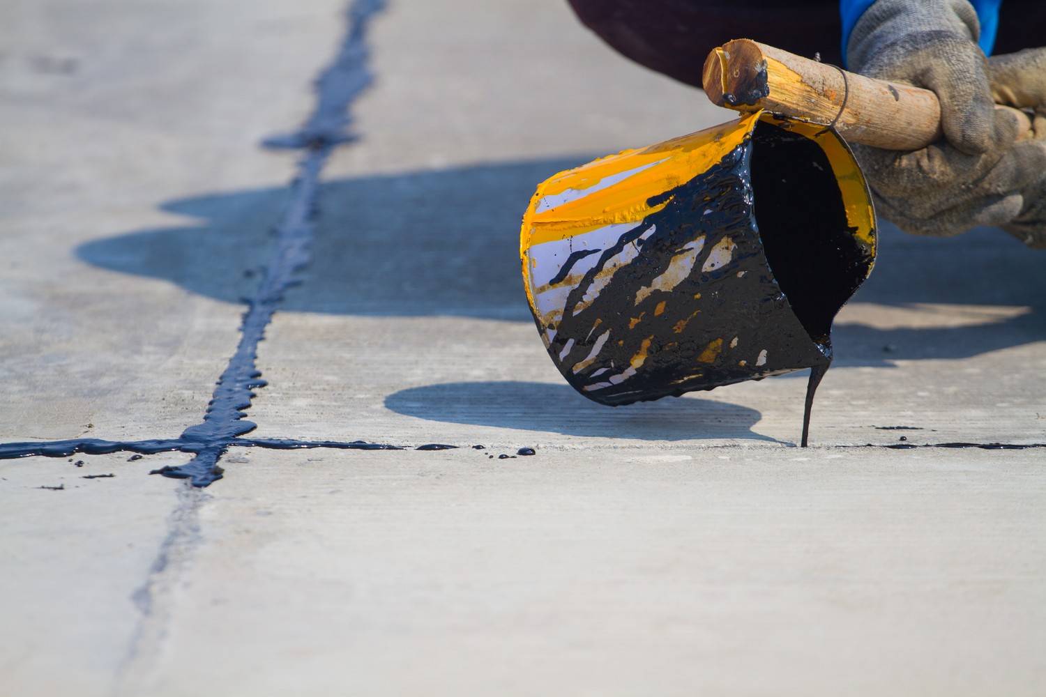 Contractor pouring liquid hot rubberized sealant to repair pavement cracks during maintenance